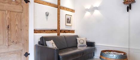 A room with a wooden door, a leather sofa, a wall-mounted light fixture, and a wooden barrel table.