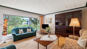 A living room with a sofa, a coffee table, a lamp, a television, and a large window with a view of greenery. - Holiday Apartment 'No. 10' with Mountain View and Private Terrace; additional dogs upon request (Bad Wildbad)