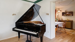 A grand piano in a room with a wooden floor, a dining table with chairs, and a kitchen area with cabinets and a hanging light fixture. - Holiday Apartment 'No. 10' with Mountain View and Private Terrace; additional dogs upon request (Bad Wildbad)