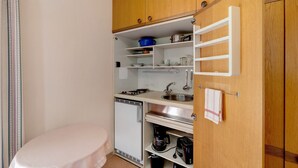 Pieni, käytännöllinen keittiö, jossa on pesuallas, liesi ja säilytystilaa tarjoavat hyllyt.