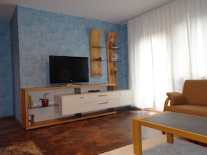 A living room with a flat-screen TV, wooden shelves, a sofa, and a coffee table. - Apartment 'Mühlengrün' with Mountain View, Balcony and Wi-Fi (Oberwolfach)