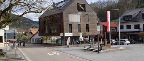 A modern building with large windows, a visible entrance, and a street in front.