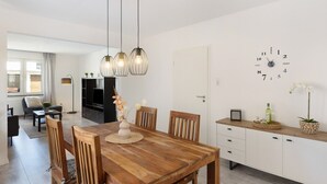Een moderne woonruimte met een houten eettafel, stoelen, een televisie en een wandklok.