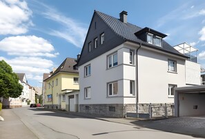 Een woonstraat met moderne huizen, een heldere lucht en een rode auto langs de kant van de weg.