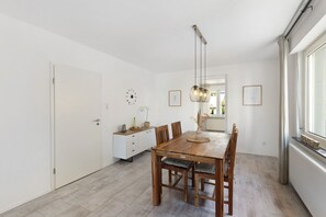 Een eetgedeelte met een houten tafel, stoelen, een hanglamp en een wit kastje.
