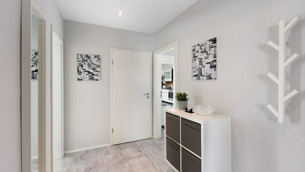 Een hal met een witte deur, een console tafel met een plant en twee kunstwerken aan de muur.