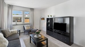 Een moderne woonkamer met een bank, salontafel, televisie en een raam met gordijnen.
