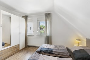 A bedroom with a bed, a wardrobe, a window with curtains, and a bedside lamp.