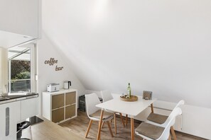 A modern kitchen with white cabinets, a coffee bar sign, a dining table with chairs, and a view through a window. - Apartment 'Dachgeschoss' with Balcony and Wi-Fi (Arnsberg)