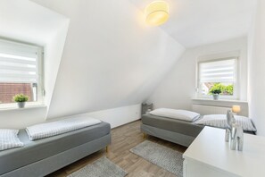 Ein modernes, gut beleuchtetes Zimmer mit zwei grauen Sofas, einem weißen Schreibtisch und einem kleinen Topfpflanzen am Fenster.