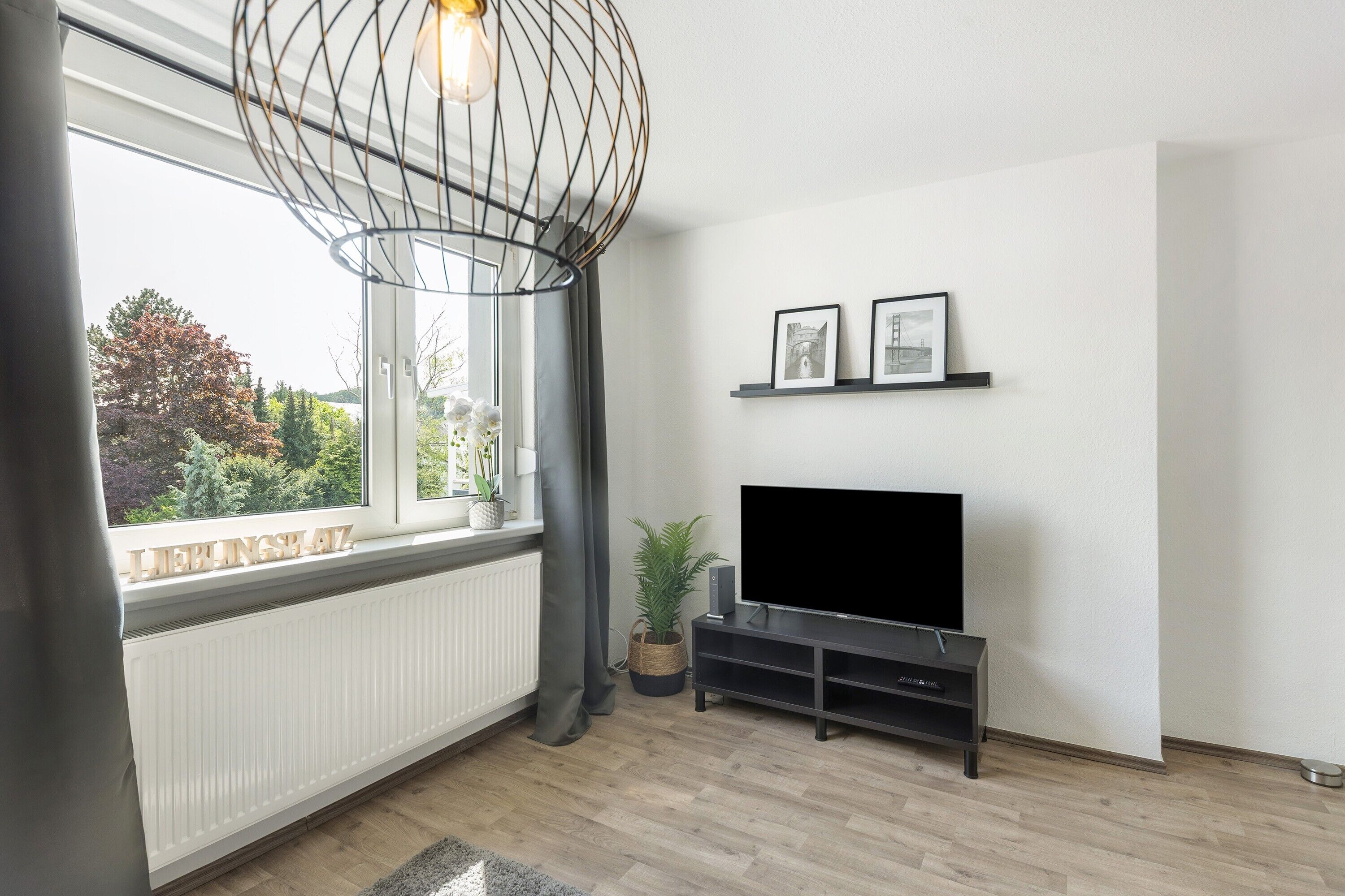 Ein modernes Wohnzimmer mit großem Fenster, einem Flachbildfernseher und einer dekorativen Leuchte.