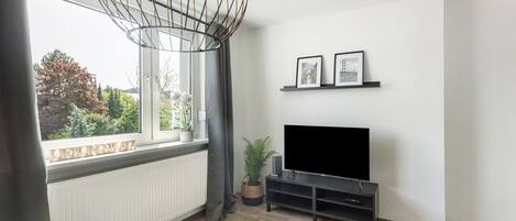 Ein modernes Wohnzimmer mit großem Fenster, einem Flachbildfernseher und einer dekorativen Leuchte.
