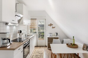 A modern kitchen with a coffee bar, a dining area, and a view through a glass door.