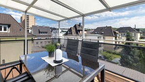 Ein Balkon mit Glastisch, Stühlen, einer Topfpflanze und einem weißen Gegenstand auf dem Tisch.