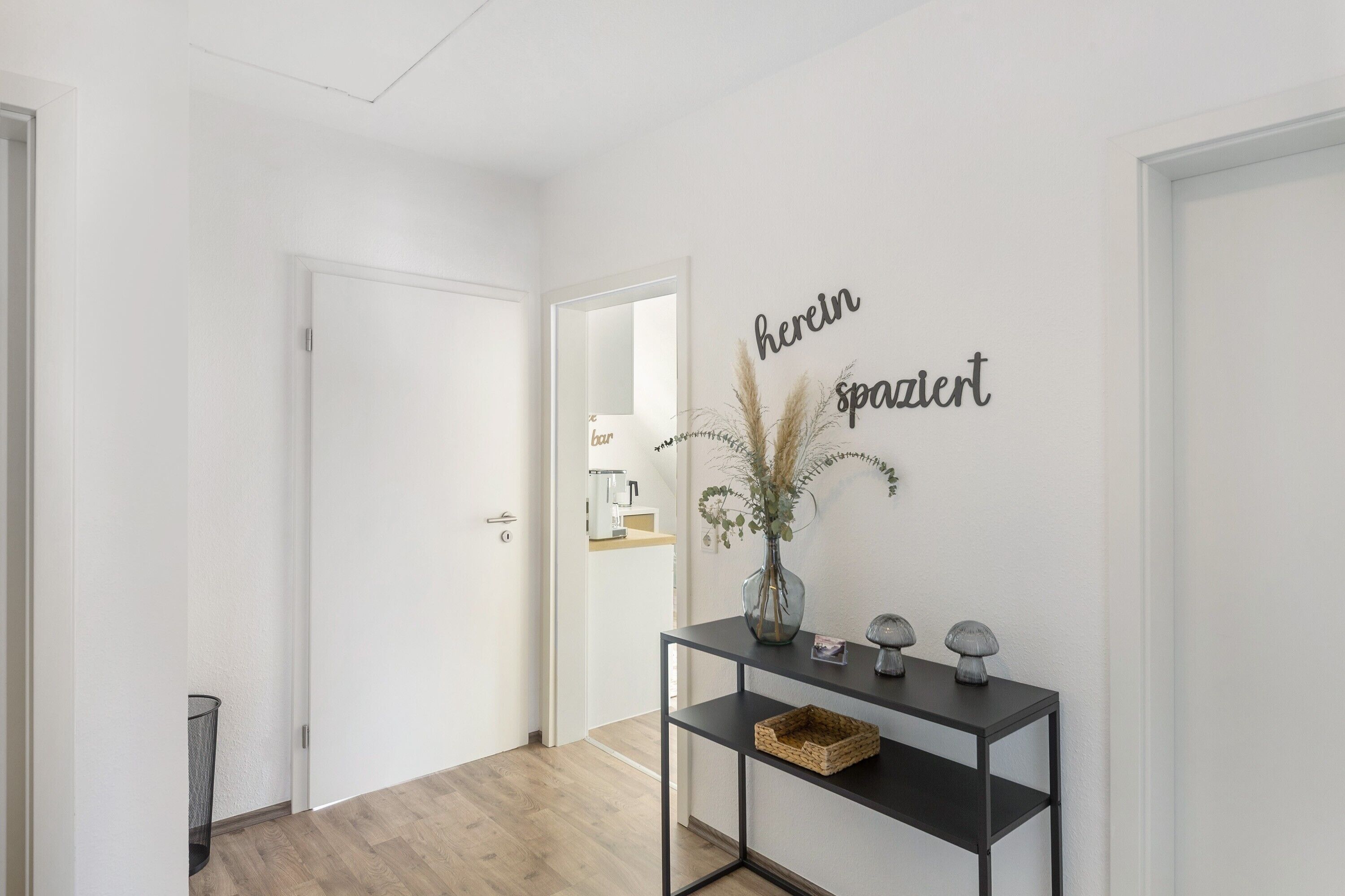 Un couloir avec une console noire, un vase contenant des plantes séchées et une enseigne murale sur laquelle on peut lire : « Ici, espace détente ».