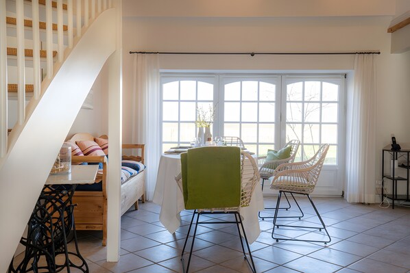 A dining area with a table, chairs, and a view through large windows.