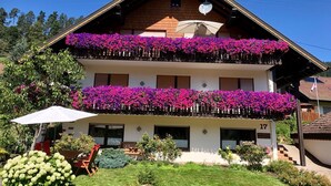 A two-story building with balconies adorned with flowers, a visible number '17', and a garden area with a table and chairs. - Apartment 'Kaltenbach' with Balcony and Wi-Fi (Enzklösterle)
