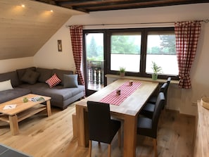 Una sala acogedora con un sofá, una mesa de comedor de madera y un balcón con plantas.
