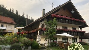 A traditional chalet with a balcony, a garden with flowers, and a paved driveway. - Apartment 'Kaltenbach' with Balcony and Wi-Fi (Enzklösterle)
