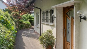 Een pad dat leidt naar een huis met een deur en ramen, omgeven door groen.