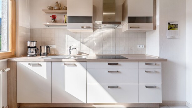 Een moderne keuken met witte kasten, roestvrijstalen apparatuur en een raam dat voor natuurlijk licht zorgt.