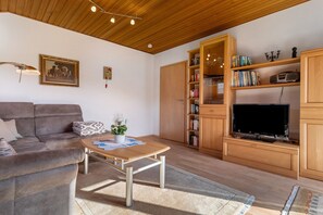 Una sala de estar con sofá, mesa de centro, aparador de madera, estantería y televisor.