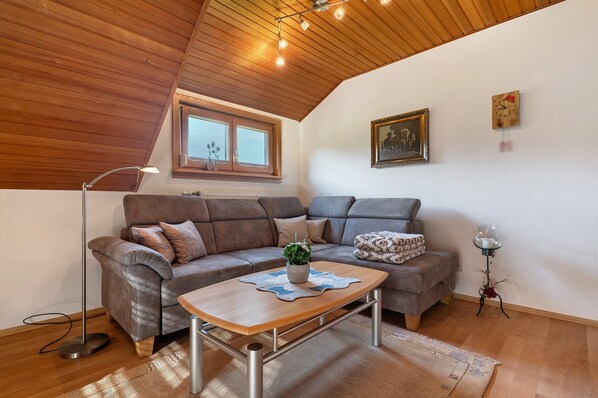 Ein gemütliches Wohnzimmer mit Holzboden, einer Sofagarnitur, einem Couchtisch mit Pflanze und einer Stehlampe.