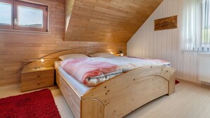 Een slaapkamer met een schuine plafond, houten wanden, een bed met een rode mat en een raam met gordijnen.