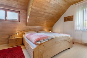 Un dormitorio con techo inclinado, paredes de madera, una cama con alfombra roja y una ventana con cortinas.