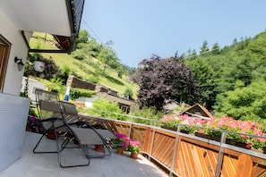 Un balcon avec une table et des chaises, une clôture en bois et une vue sur une colline verdoyante parsemée de fleurs.