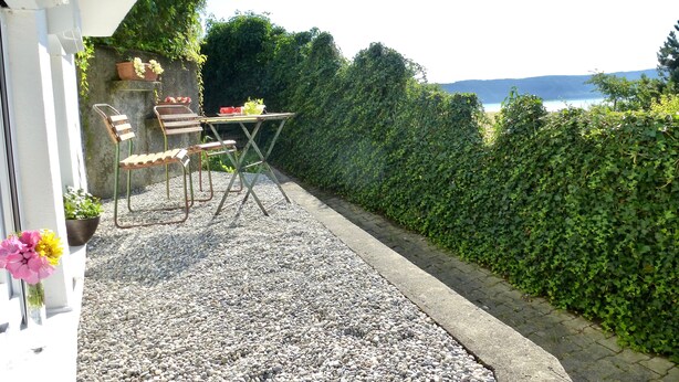 An outdoor seating area with a table and chairs, surrounded by a gravel path and a hedge. - Lake Constance Bliss Apartment with Private Terrace (Überlingen)