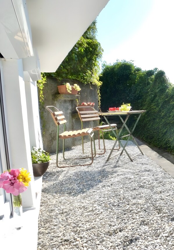 An outdoor seating area with a table and chairs, surrounded by gravel and greenery.