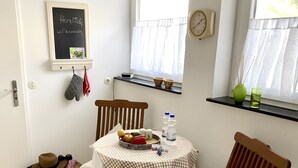 A cozy room with a wooden chair, a table with a checkered tablecloth, a fruit bowl, a clock, and a window with curtains. - Lake Constance Bliss Apartment with Private Terrace (Überlingen)