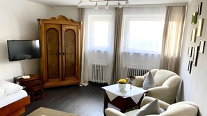 A hotel room with a bed, a TV, a wooden wardrobe, a sofa, a small table with a vase, and a radiator. - Lake Constance Bliss Apartment with Private Terrace (Überlingen)