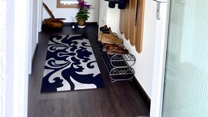 A hallway with a ceiling light, a door with a metal grill, a potted plant, a wall-mounted coat rack, and a patterned rug. - Lake Constance Bliss Apartment with Private Terrace (Überlingen)