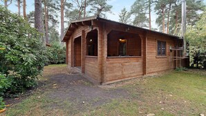 A wooden cabin with a porch, surrounded by trees. - Apartment 'Waldblick' with Private Terrace, Private Garden and Wi-Fi (Berlin)