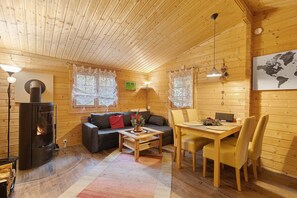 Ein gemütliches Blockhaus-Interieur mit Holzausstattung, einer Couch, einem Esstisch mit Stühlen, einem Kamin und einer Weltkarte an der Wand.