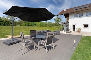 An outdoor patio with a table and chairs, a large umbrella, and a house in the background.