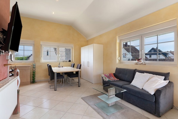 A modern living room with a dining area, a sofa, and a TV.