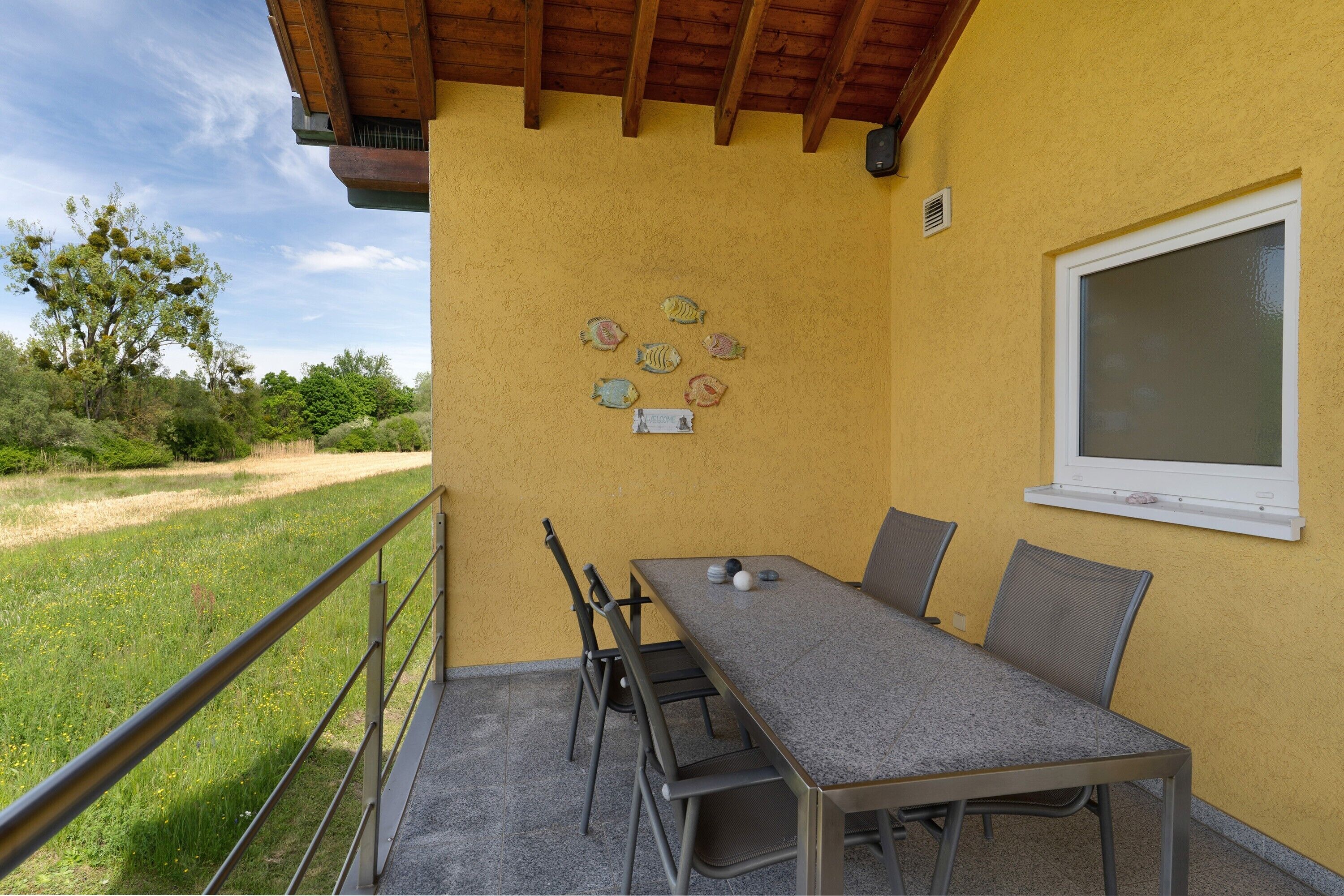 A covered patio with a table and chairs, a window, and a wall-mounted fish decoration.
