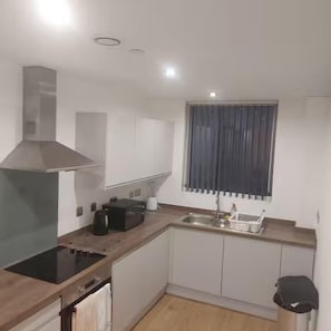 A compact kitchen with a built-in stove, a range hood, a window with curtains, and a sink. - Central 1 Bed-self Checkin, Min-arena, 7d-discount (Manchester)