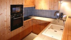 Een keuken met houten kastjes, een inbouwoven, een spoelbak en een betegelde spatwand.
