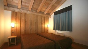 Een kamer met twee bedden, houten wanden, een klein tafeltje en twee wandlampen.