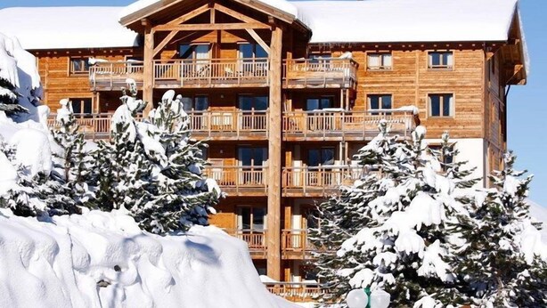 Een meerlaags houten gebouw met balkons, omgeven door met sneeuw bedekte bomen.