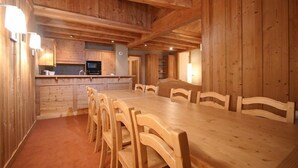 Een houten interieur met een grote eettafel en stoelen, een keukenhoek met een magnetron, en houten wanden.