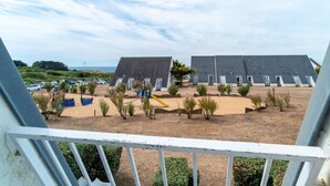 A view of a beachside property with multiple chalet-style buildings, a sandy area with small plants, and a playground.