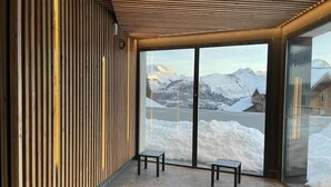 A modern interior with a wooden slatted wall, two black benches, and a glass door leading to a snowy mountain view.