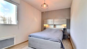 Une chambre moderne avec un grand lit, une tête de lit intégrée, des lampes de chevet et une fenêtre donnant sur la forêt.