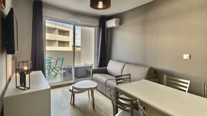Un salon moderne avec un canapé, une table à manger et des chaises. Il y a un balcon d’où l’on peut admirer la vue sur les immebles.