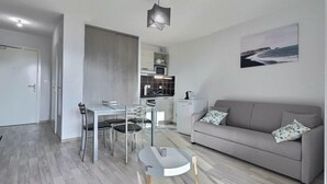 Ein modernes Wohnzimmer mit grauem Sofa, einem Esstisch mit Stühlen und einer Küchenzeile im Hintergrund.